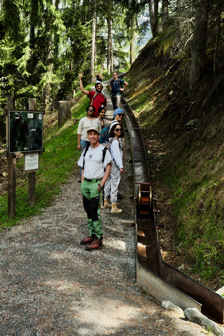 Lab members on a forest hiking trail beside a wooden water channel, smiling at the camera.
