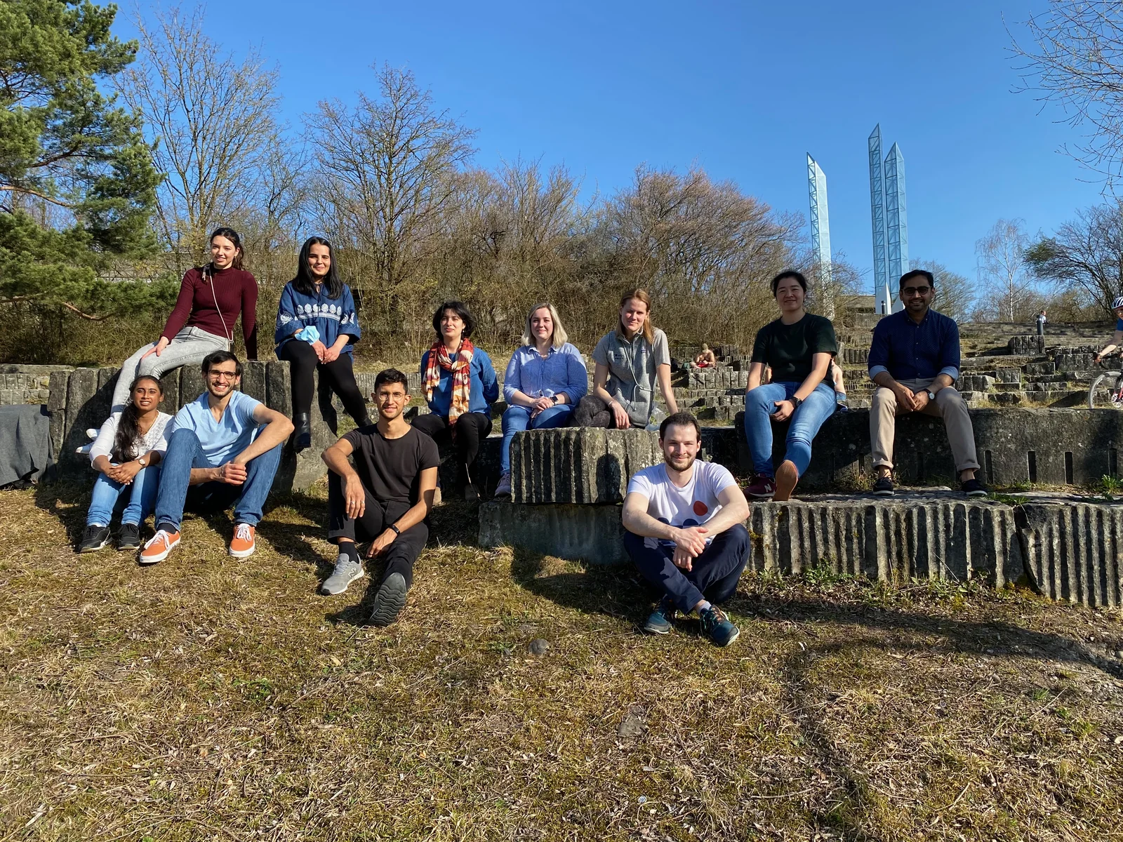 Lab members seated together on stone steps outdoors on a sunny day.